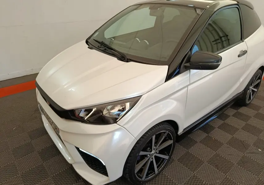 Vue 3/4 avant droite de l'AIXAM Ambition 0.5 City Coupe GTI blanche avec toit noir et rétroviseur droit noir.