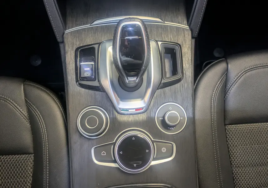 Vue plongeante sur la console centrale noire de l'Alfa Romeo Stelvio Sprint 2023 avec levier de vitesse et commandes circulaires.