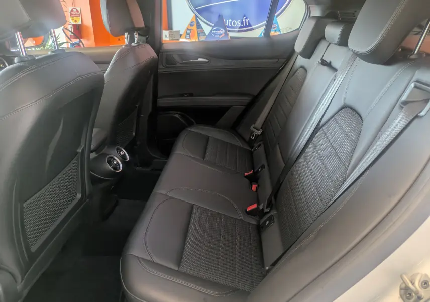 Vue latérale droite de l'intérieur arrière de l'Alfa Romeo Stelvio blanc, sièges en cuir noir et aérateurs centraux visibles.
