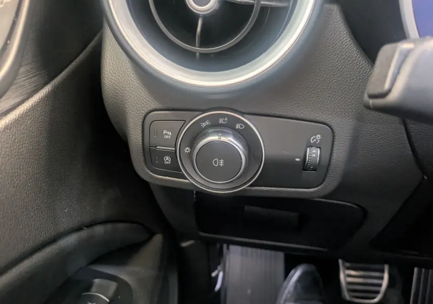Gros plan sur le bouton de commande des phares et la ventilation côté gauche de l'Alfa Romeo Stelvio blanc 2023.