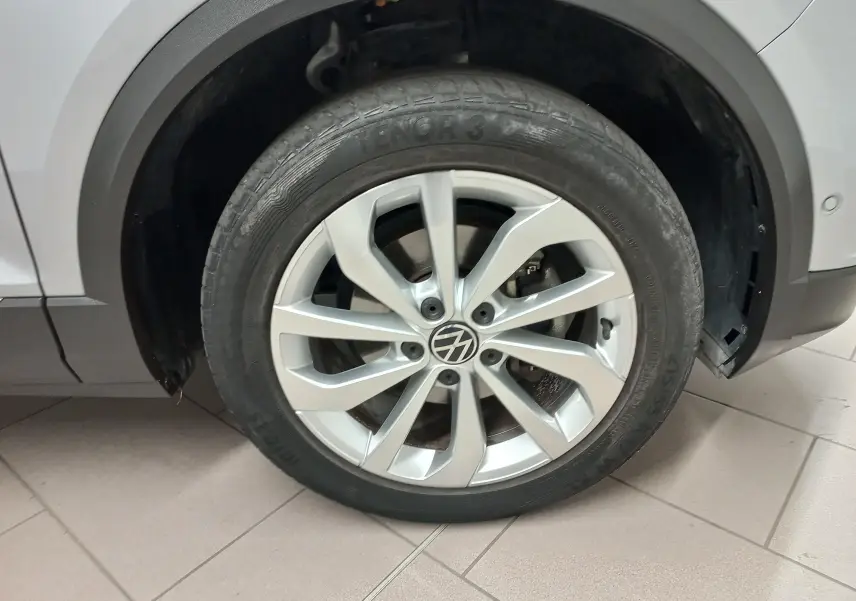 Gros plan sur la roue avant droite du Volkswagen T-Roc gris pyrite avec jante alliage et logo VW visible.
