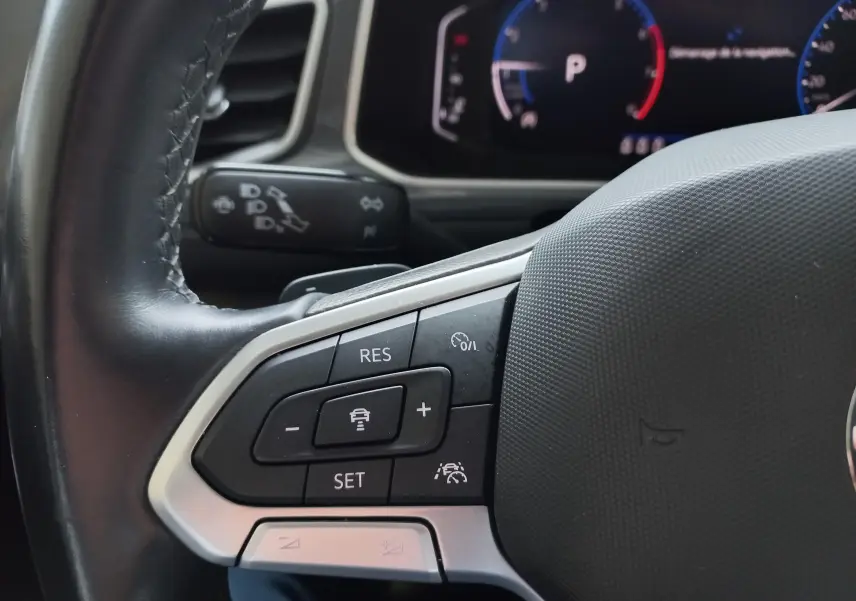 Gros plan sur les commandes au volant du Volkswagen T-Roc 1.5 TSI 150 DSG7 Style, avec tableau de bord numérique en arrière-plan.
