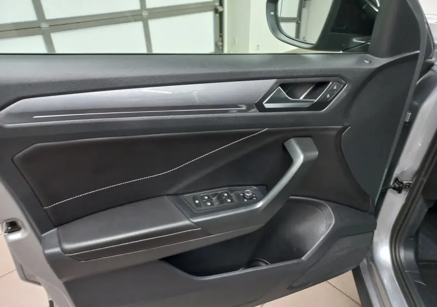 Vue intérieure côté gauche de la porte avant d'un Volkswagen T-Roc 1.5 TSI gris Pyrite avec surpiqûres blanches.