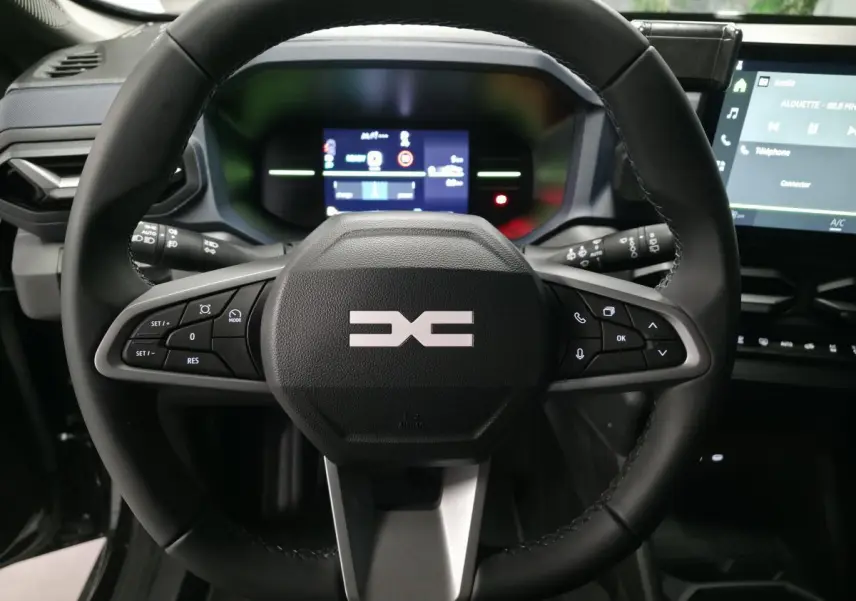 Vue intérieure centrée sur le volant noir du Dacia Duster 1.6 Hybrid 2025 avec commandes multifonctions et tableau de bord digital.