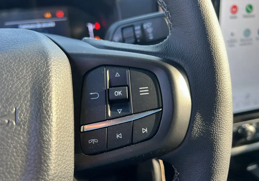 Gros plan sur les commandes multifonctions du volant cuir du Ford Ranger 2025, intérieur noir avec écran tactile visible.