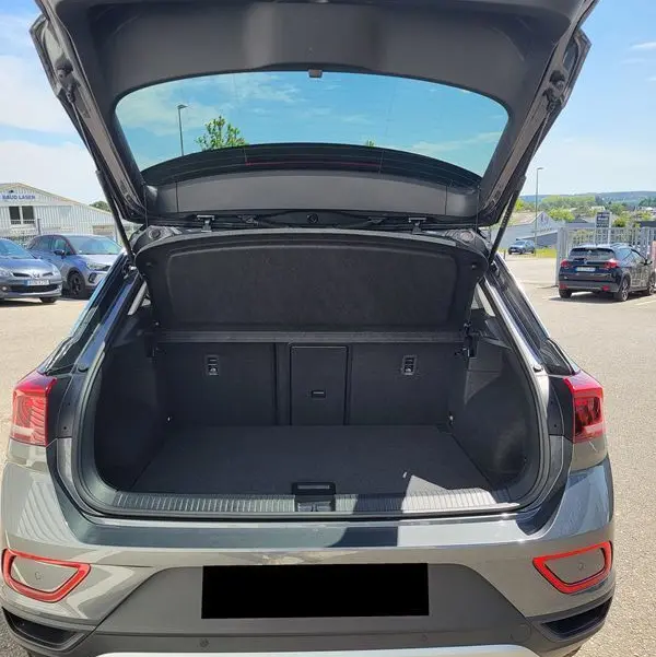 Vue arrière du Volkswagen T-Roc gris Indium 2025 avec coffre ouvert et intérieur spacieux visible en extérieur.