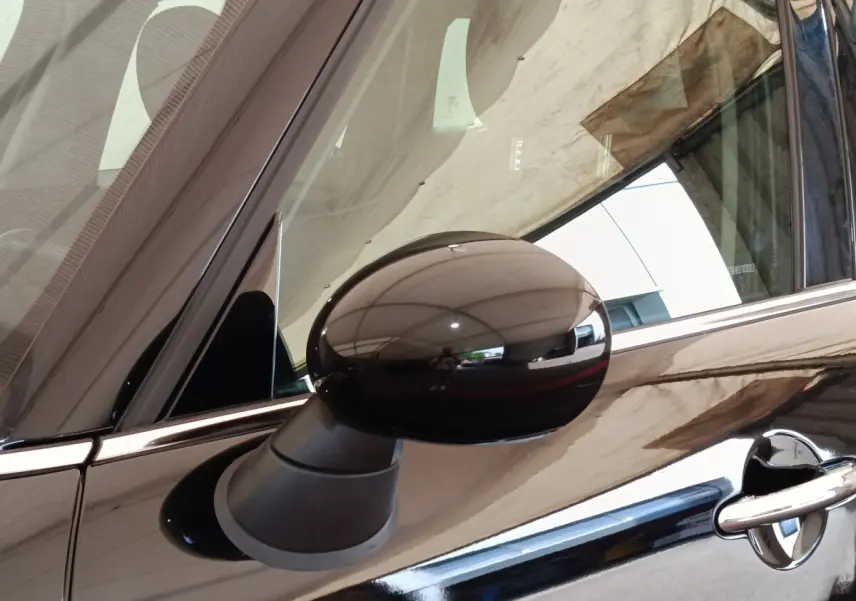 Gros plan sur le rétroviseur côté gauche noir brillant d’un MINI Countryman Cooper 2019 noir, avec reflet de l’environnement.