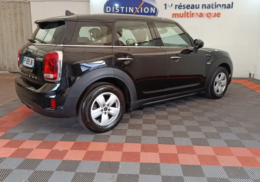 Vue 3/4 arrière droit d'une MINI Countryman noire stationnée en intérieur, avec jantes argentées et logo Cooper visible.