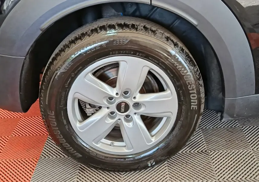 Gros plan sur la roue avant droite d'une MINI Countryman noire, jante argentée à cinq branches, pneu Bridgestone.