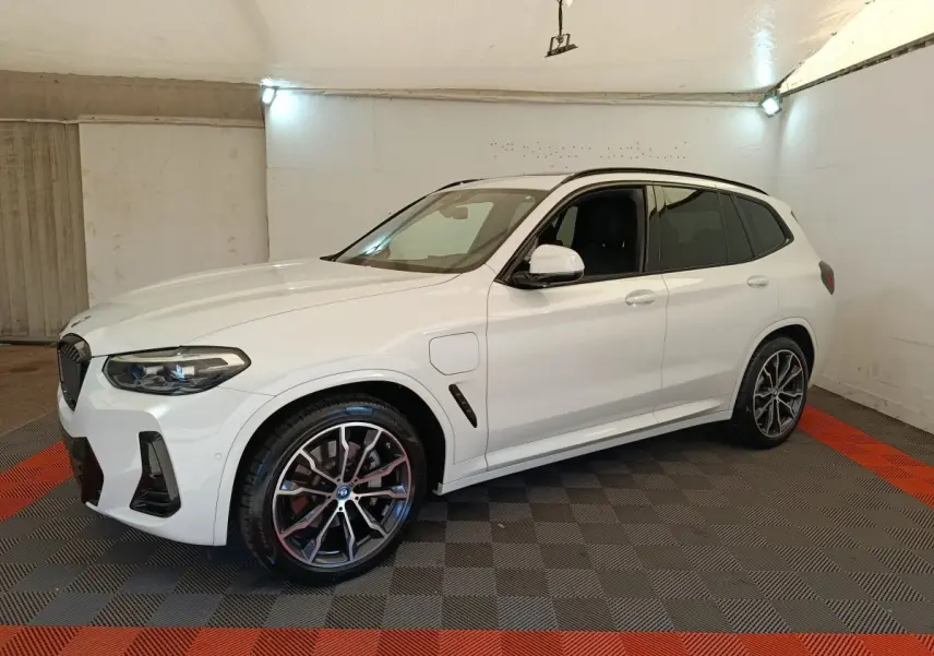 BMW X3 xDrive30e blanc en 3/4 avant droit, avec jantes alliage et prises de recharge latérales visibles.