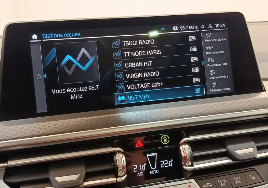 Affichage tactile central du tableau de bord du BMW X3 blanc, montrant les réglages radio et climatisation.