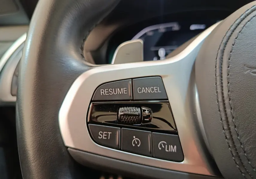 Gros plan sur les commandes de régulateur de vitesse au volant cuir d'une BMW X3 blanc, version 2023.