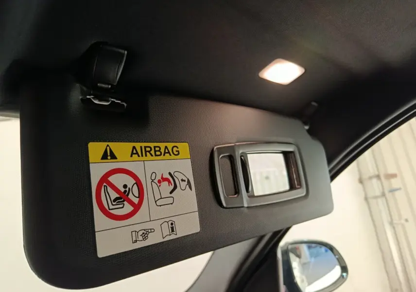 Pare-soleil intérieur noir avec miroir intégré et étiquette d'avertissement airbag, côté conducteur BMW X3 blanc visible au rétro.
