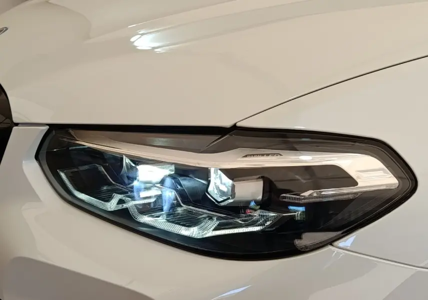 Gros plan sur le phare avant droit LED d’un BMW X3 xDrive30e blanc, mettant en valeur ses détails lumineux modernes.