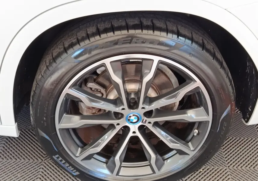 Gros plan sur la roue avant droite d’un BMW X3 blanc avec jante alliage gris foncé et logo M Sport.