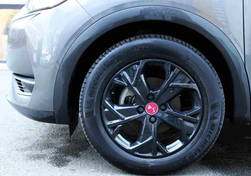 Gros plan sur la roue avant gauche du DS3 Crossback gris platinium, jante noire brillante avec logo rouge DS au centre.