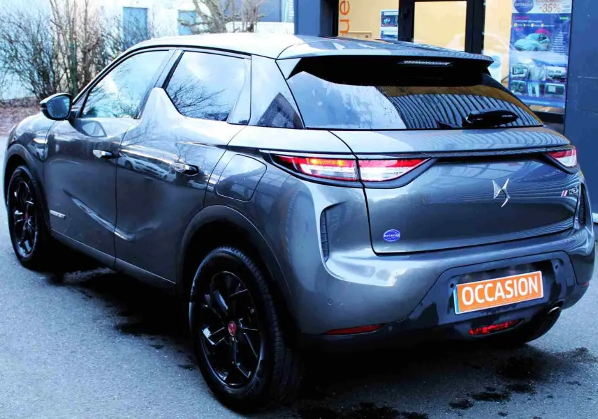 Vue 3/4 arrière droite du DS3 Crossback gris platinium métallisé avec jantes noires et feux arrière allumés.