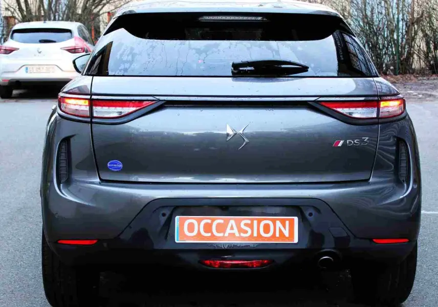Vue arrière d'un DS3 Crossback gris platinium métal avec feux allumés et plaque d'occasion visible.