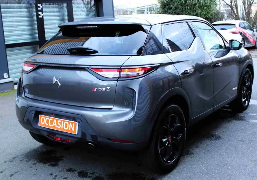Vue 3/4 arrière droite d’un DS3 Crossback gris platinium métal avec jantes noires et feux arrière allumés.