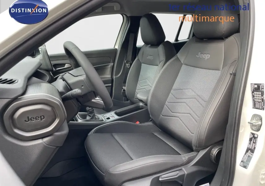 Vue intérieure côté conducteur du Jeep Avenger blanc neige 2024, sièges noirs en cuir et tissu avec logo Jeep brodé.