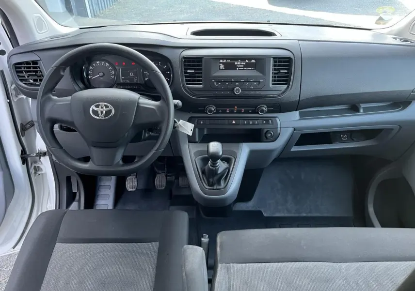 Vue intérieure avant du Toyota Proace Fourgon blanc 2021, tableau de bord avec volant, boîte manuelle et écran central simple.
