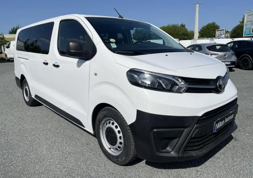 Vue 3/4 avant d'un Toyota Proace Fourgon blanc avec pare-chocs noirs et jantes acier 16 pouces sur parking.