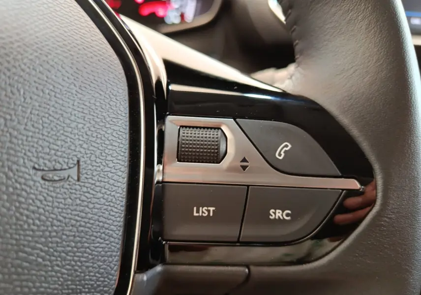 Gros plan sur les commandes multifonctions noires du volant cuir d’une Peugeot 208 blanche, version PureTech 75 S&S Style 2023.