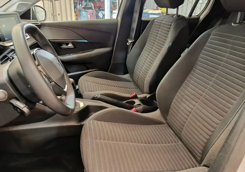 Vue intérieure côté conducteur de la Peugeot 208 PureTech 75 S&S Style 2023, sièges tissu gris et volant cuir.