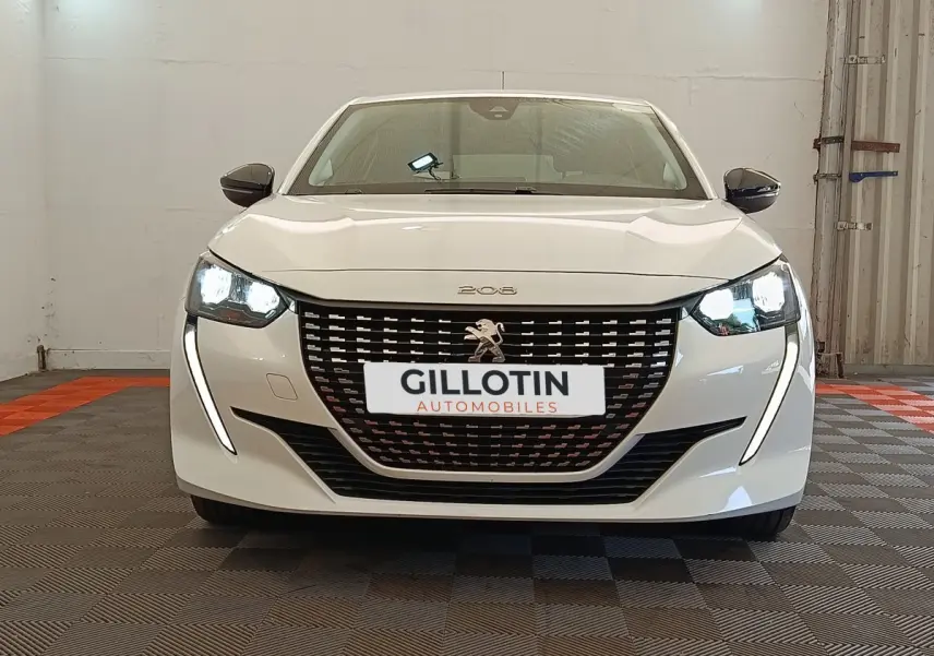 Vue frontale d'une Peugeot 208 blanche 2023 avec phares LED allumés et calandre noire distinctive.