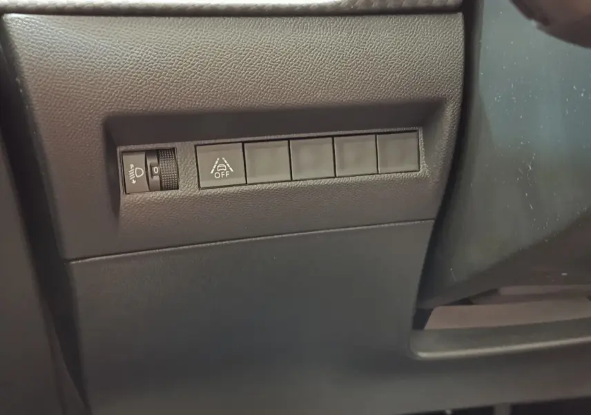 Vue rapprochée des commandes de réglage des phares et de l'alerte de franchissement de ligne sur Peugeot 208 blanc 2023.