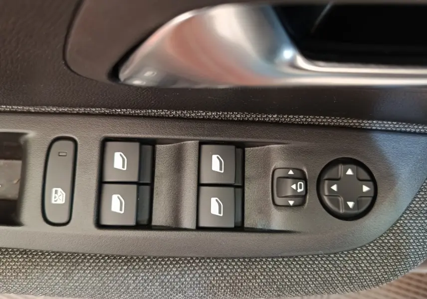 Gros plan sur les commandes des vitres et rétroviseurs côté conducteur d'une Peugeot 208 blanche de 2023.