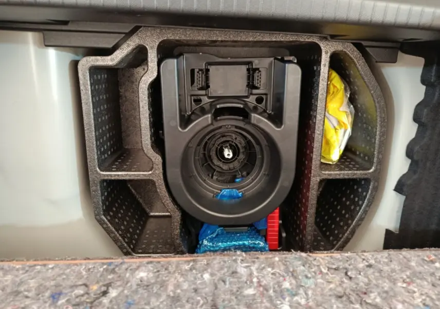 Vue rapprochée du compartiment de rangement sous le plancher de coffre d'une Peugeot 208 blanche, 2023.