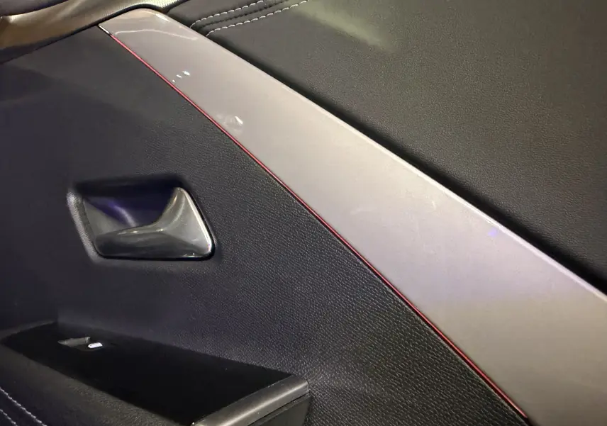 Détail intérieur de la porte avant droite de l’Opel Astra gris, avec surpiqûres rouges et poignée chromée.
