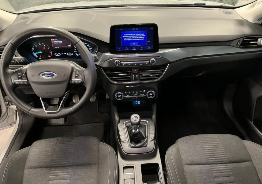 Vue intérieure avant de la Ford Focus 1.0 EcoBoost 2021 avec tableau de bord noir et console centrale équipée d'une boîte manuelle.