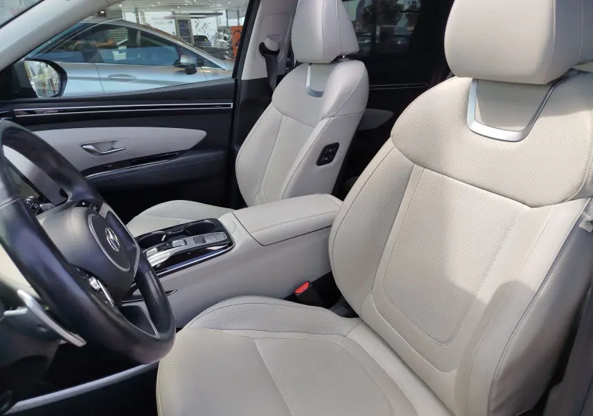 Vue intérieure côté conducteur du Hyundai Tucson 2021, sièges cuir beige clair avec console centrale et volant visibles.