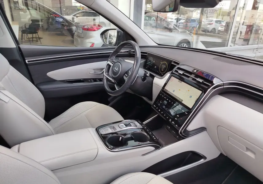 Vue intérieure côté conducteur du Hyundai Tucson 2021, avec sièges cuir clairs et tableau de bord moderne à écran tactile.