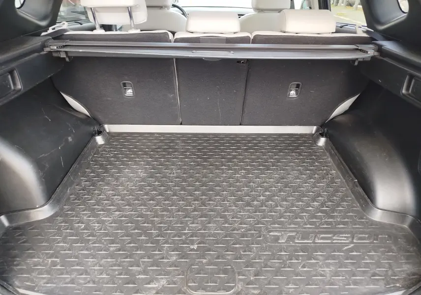 Vue intérieure du coffre du Hyundai Tucson 2021, avec tapis de protection noir marqué Tucson et sièges arrière beiges visibles.
