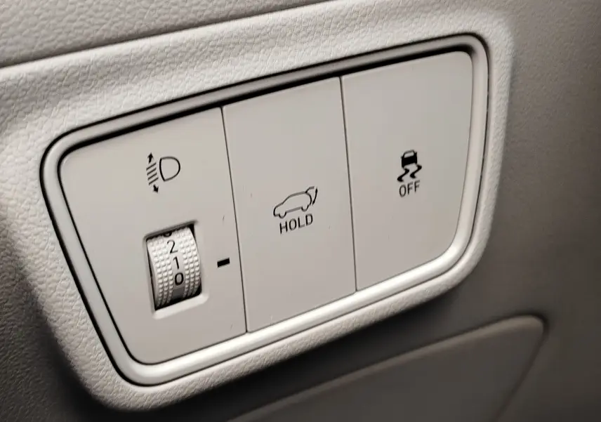Gros plan sur les commandes intérieures blanches du Hyundai Tucson 1.6 CRDI 136ch Hybride, avec réglage des phares et fonctions hold et traction.
