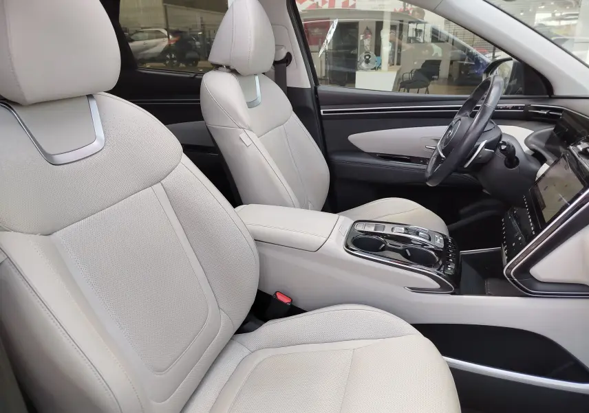 Vue intérieure côté conducteur du Hyundai Tucson 2021, sièges cuir beige clair et console centrale moderne.