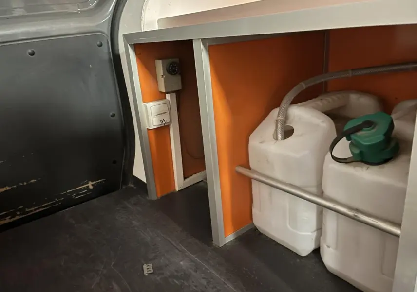 Détail intérieur du compartiment de chargement du Renault Kangoo Express gris foncé avec rangements et bidons blancs.