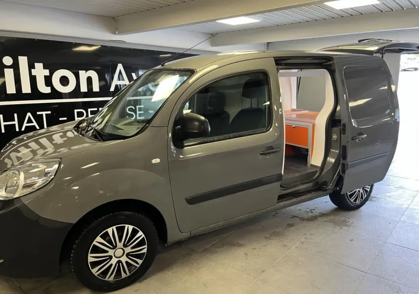 Vue 3/4 avant droit du Renault Kangoo Express gris foncé avec porte latérale droite ouverte montrant l'espace de chargement aménagé.