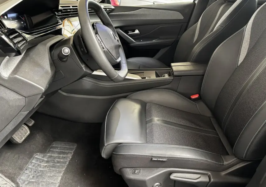 Intérieur avant droit de la Peugeot 308 gris clair 2024, siège en cuir noir avec volant multifonction et écran tactile.