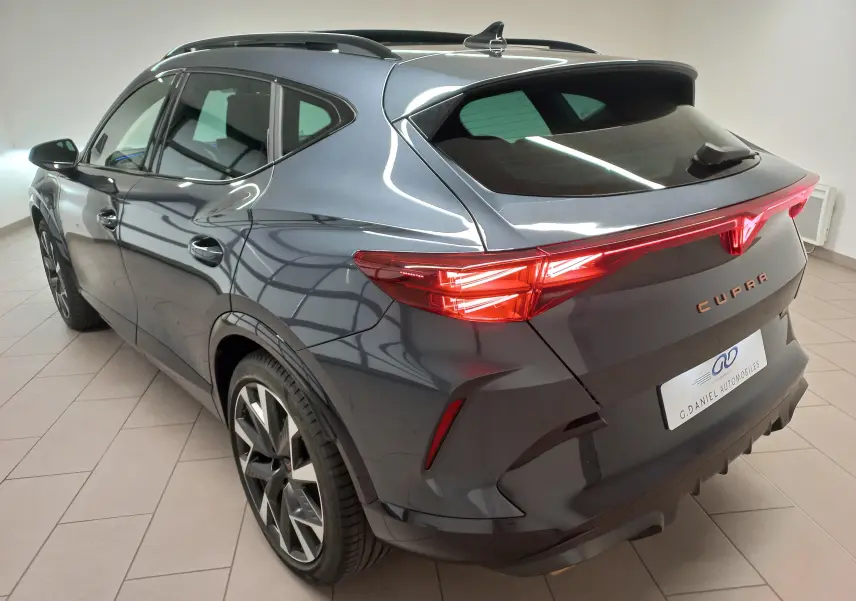 Vue 3/4 arrière droit du CUPRA Formentor gris magnétique 2025 avec toit ouvrant panoramique et feux arrière allumés.