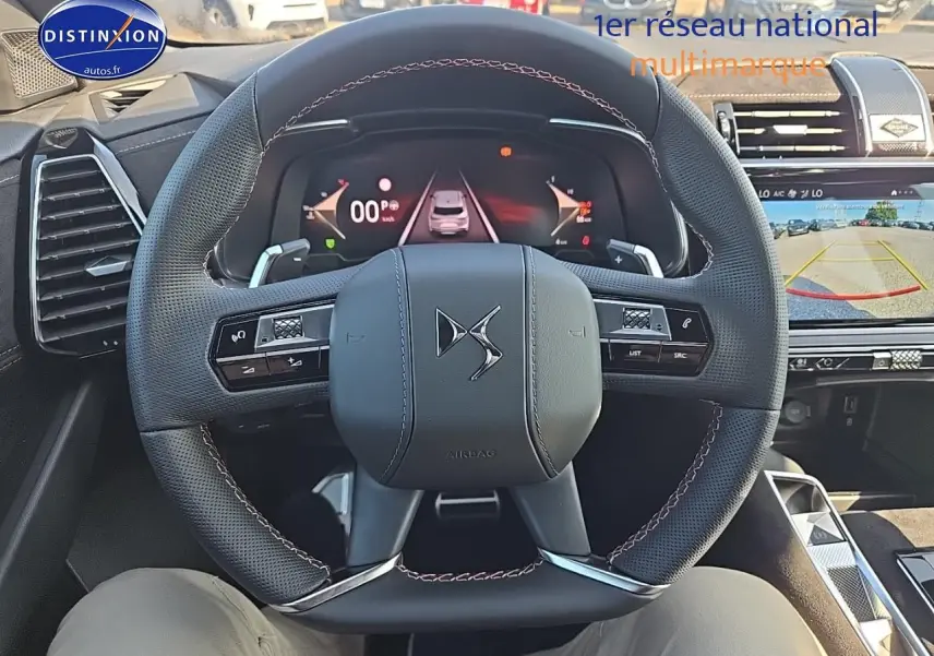 Vue intérieure centrée sur le volant DS noir avec coutures rouges et tableau de bord numérique du DS7 Cristal Pearl 2025.