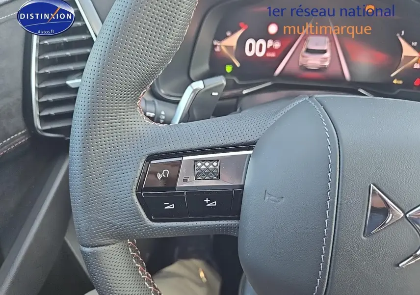 Gros plan sur le volant en cuir perforé gris du DS7 Cristal Pearl, avec commandes intégrées et tableau de bord numérique visible.