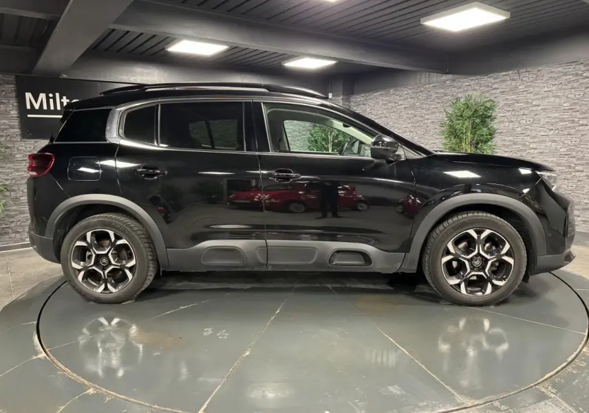 Profil côté gauche d'un SUV Citroën C5 Aircross noir nacré avec jantes alliage bi-ton dans un showroom.