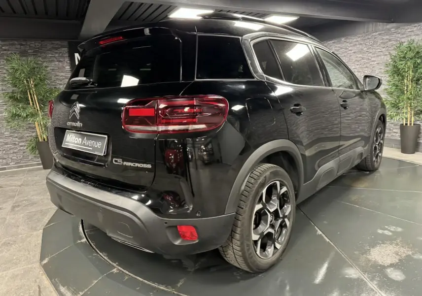 Vue 3/4 arrière droite du Citroën C5 Aircross noir nacré avec jantes bi-ton et barres de toit noires.