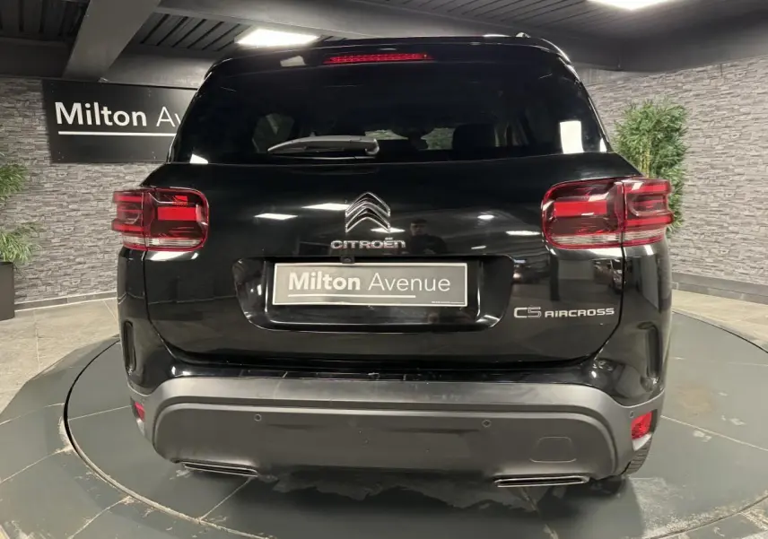 Vue arrière d'un Citroën C5 Aircross noir perla nera avec feux arrière LED et logo distinctif sur fond de showroom.