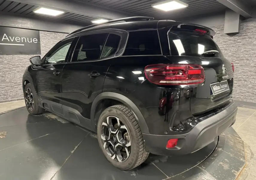 Vue 3/4 arrière droite du Citroën C5 Aircross noir nacré avec jantes bi-ton et barres de toit noires.