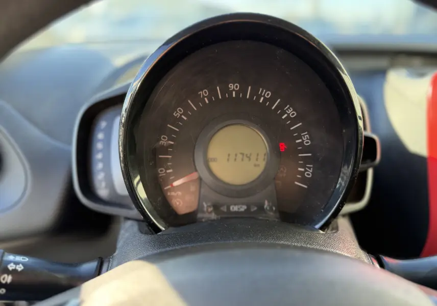 Vue rapprochée du compteur de vitesse circulaire de la Citroën C1 blanc, affichant 117411 km et témoin rouge allumé.